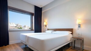 Ein Hotelzimmer mit einem großen Bett, zwei Nachttischen, einem Beistelltisch und einem Fenster mit Vorhängen.