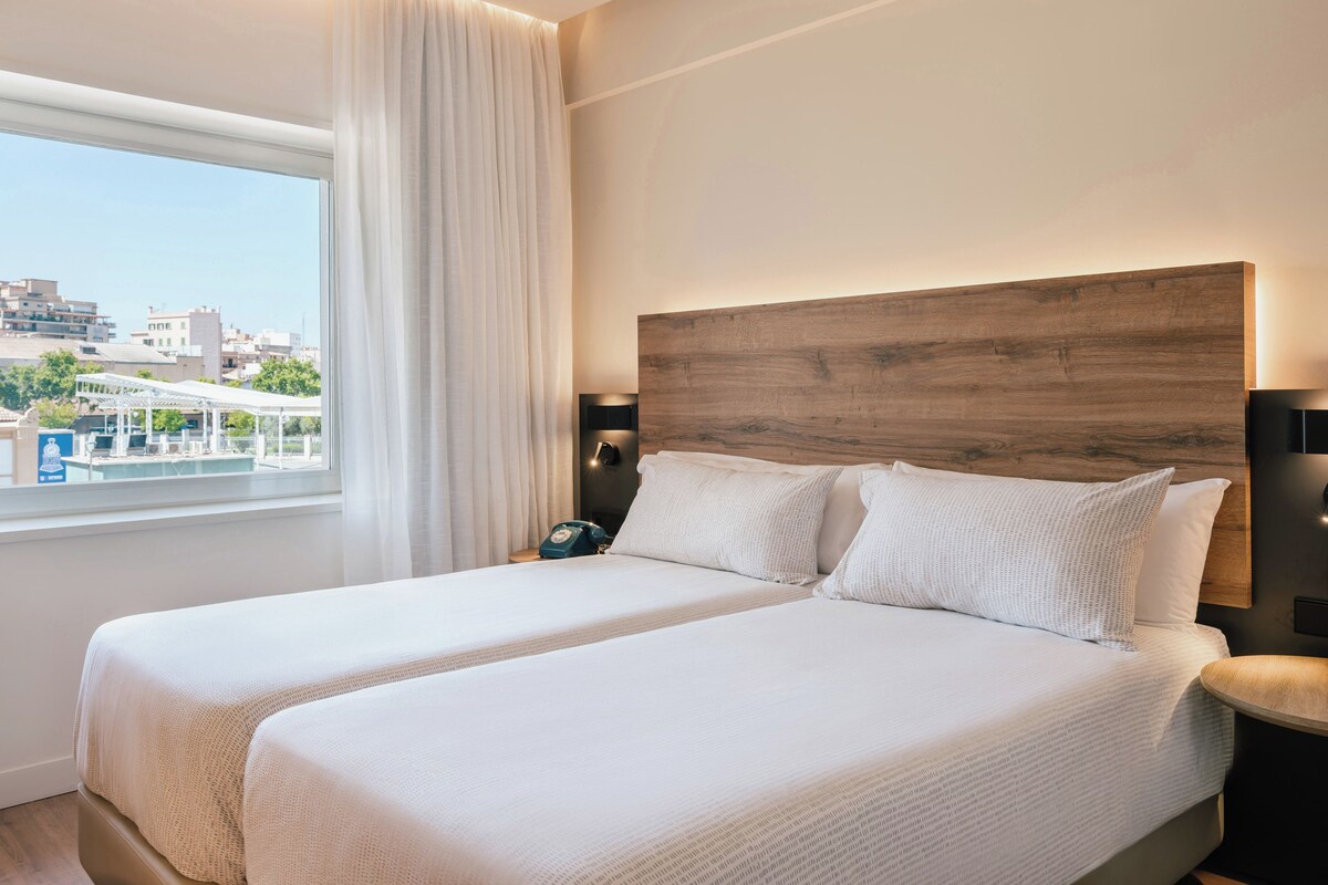 Une chambre d’hôtel avec un grand lit, une table de chevet, une lampe et une vue sur la ville.