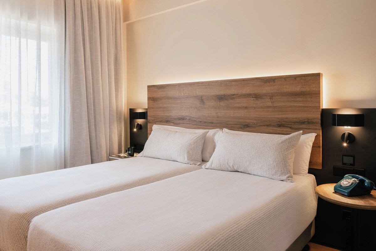 Une chambre d’hôtel avec un grand lit, une table de chevet, une lampe et une vue sur l’extérieur.
