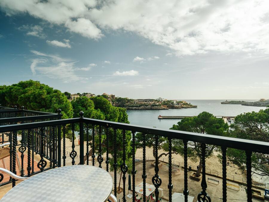 A balcony with a table and chairs, overlooking a coastal area with trees and a body of water.