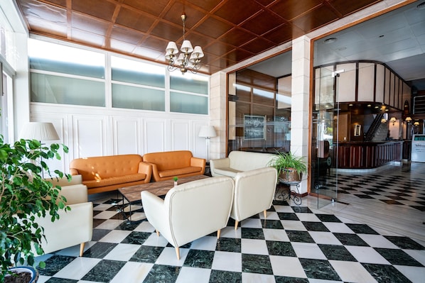 A lobby with a checkered floor, a sofa, armchairs, a chandelier, and a glass partition. - Hotel THB Felip - Adults Only (Manacor)