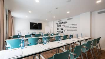 Ein Konferenzraum mit türkisfarbenen Stühlen, weißen Tischen und Wasserflaschen. An der Wand ist ein motivierendes Zitat angebracht.