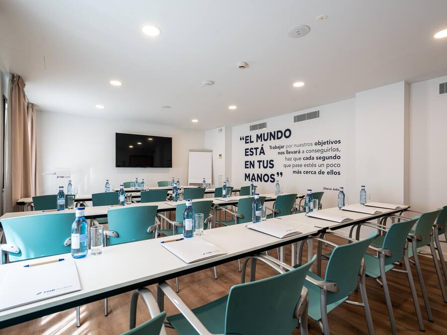 A conference room with teal chairs, white tables, and water bottles. A motivational quote is displayed on the wall.