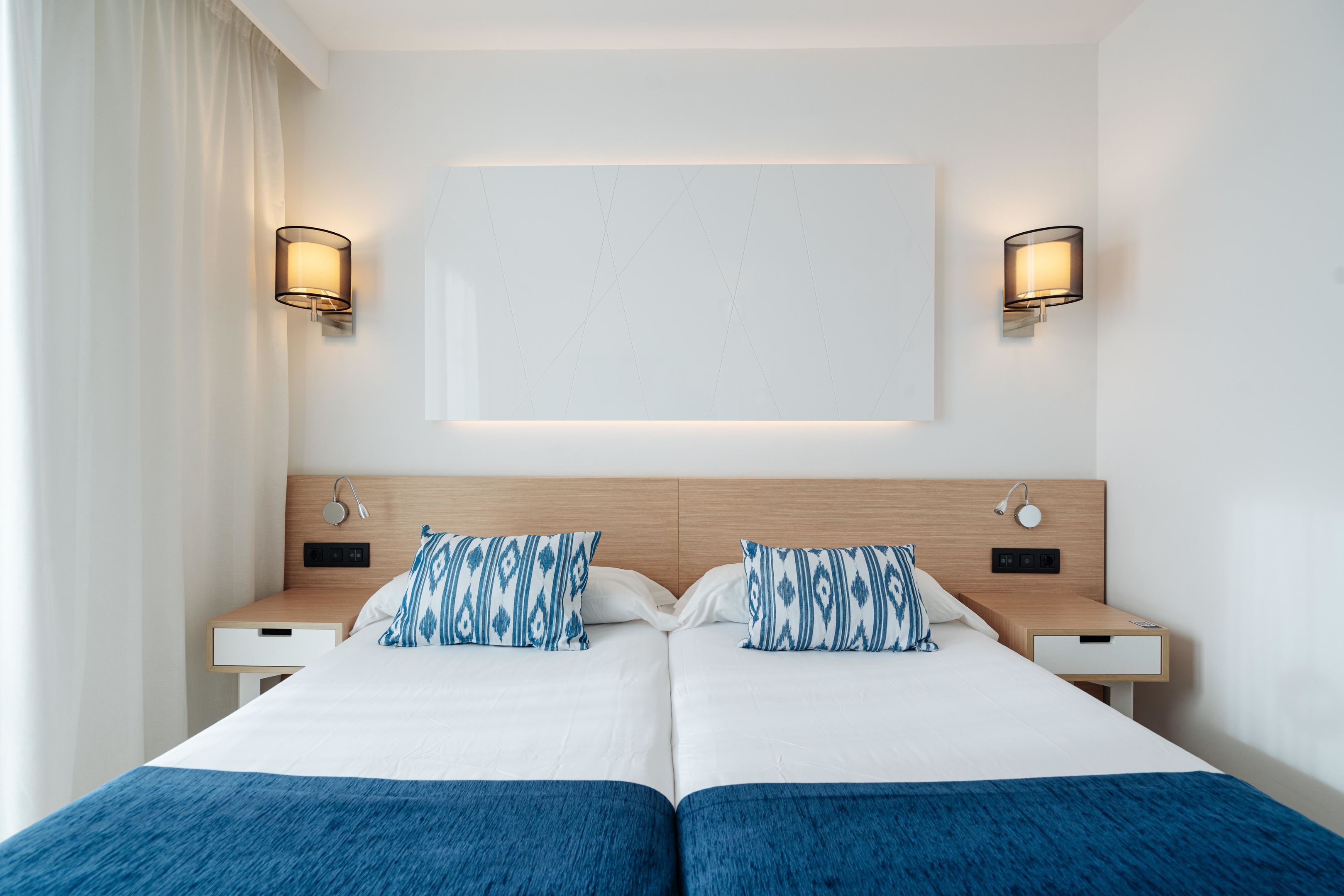 Habitación de hotel con dos camas, un espejo grande, lámparas de noche y un cabecero de madera.
