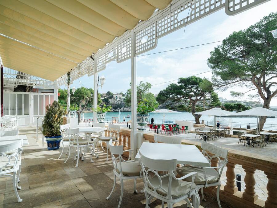 An outdoor café with white tables and chairs, a covered seating area, and a view of the sea.
