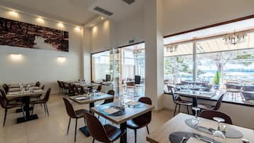 Ein Restaurant mit mehreren Tischen und Stühlen, einem großen Gemälde an der Wand und großen Fenstern mit Blick ins Freie.