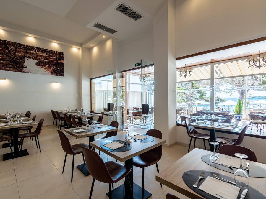 Un restaurante con varias mesas y sillas, un cuadro grande en la pared y ventanas amplias con vistas al exterior.