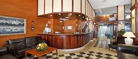 A lobby with a checkered floor, wooden paneling, a reception desk, leather sofas, and a framed picture on the wall.