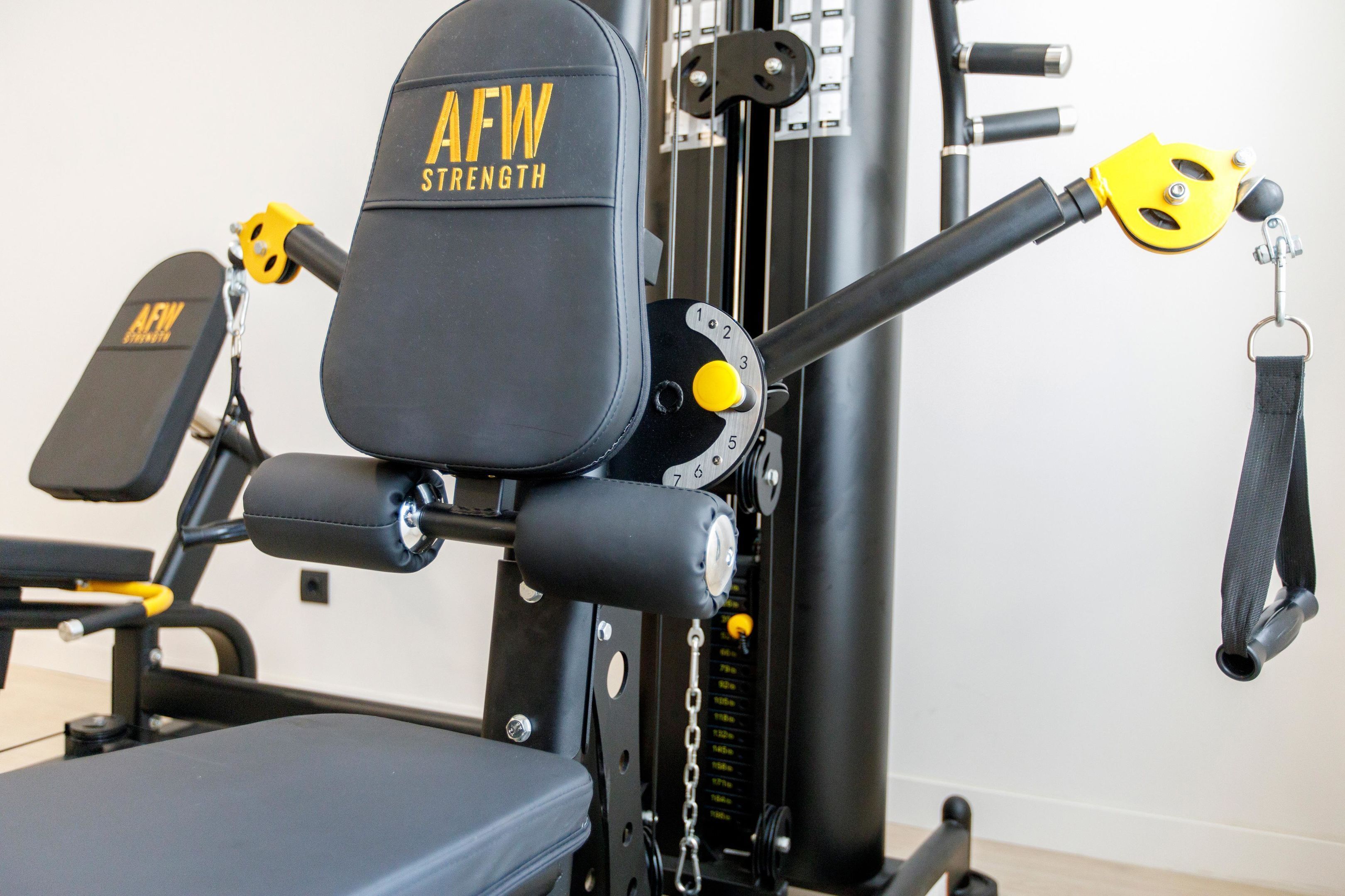 Un gimnasio con una máquina de entrenamiento de fuerza negra y amarilla con la etiqueta "AFW STRENGTH".