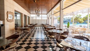 A restaurant with checkered flooring, wicker chairs, and tables set for dining. Large windows offer a view of the sea and a balcony area. - Hotel THB Felip - Adults Only (Manacor)