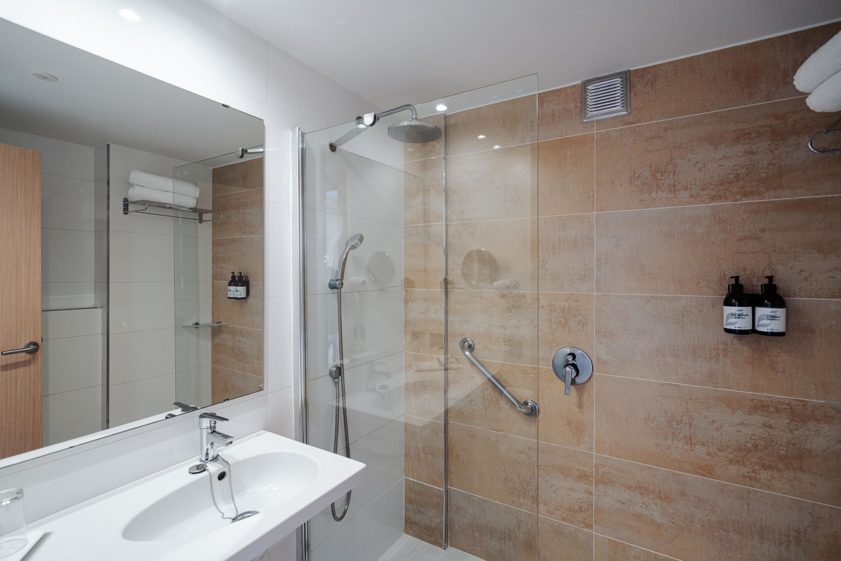 Een moderne badkamer met een douchecabine van glas, een witte wastafel en een grote spiegel.