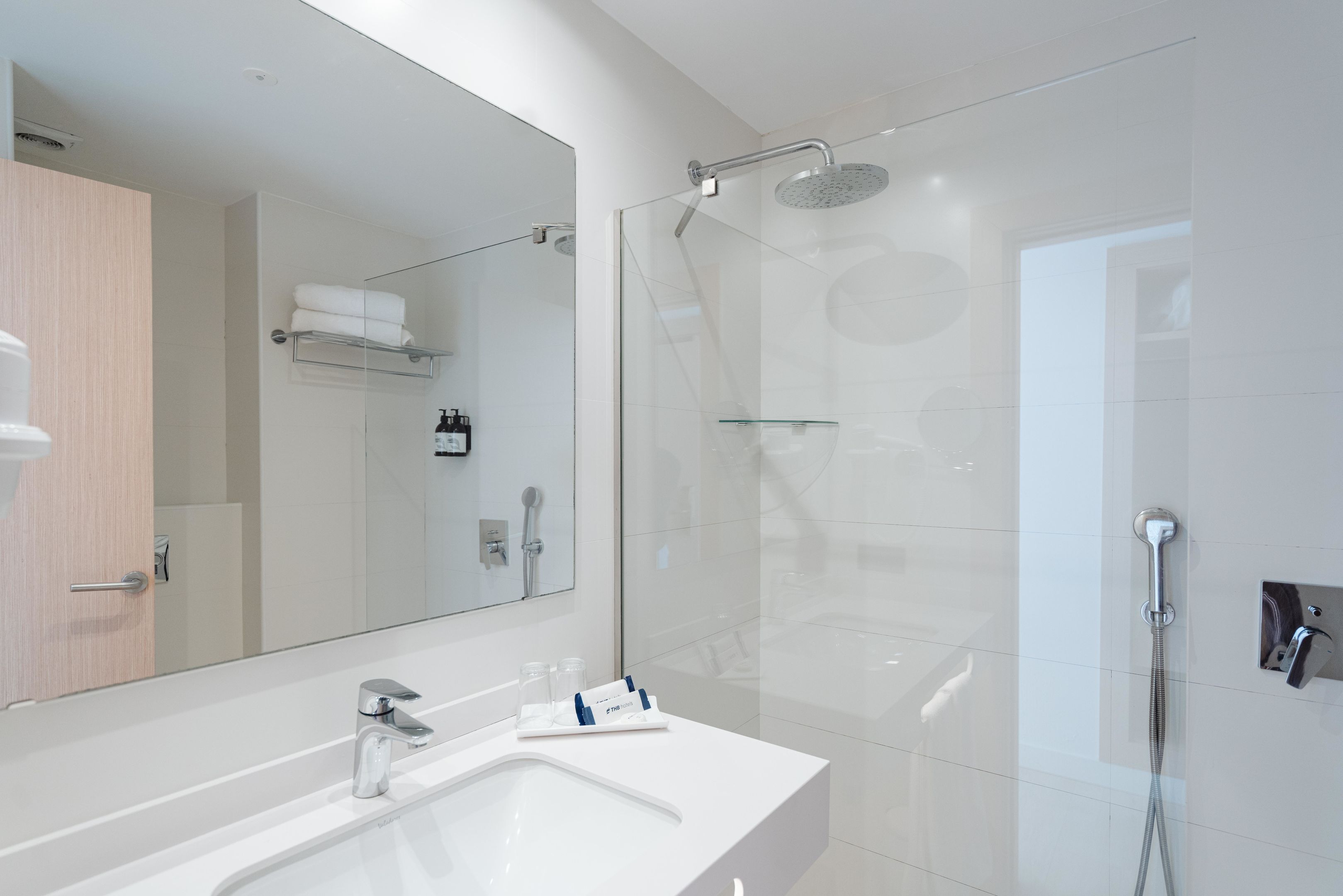 A modern bathroom with a large mirror, a white sink, and a glass-enclosed shower area.