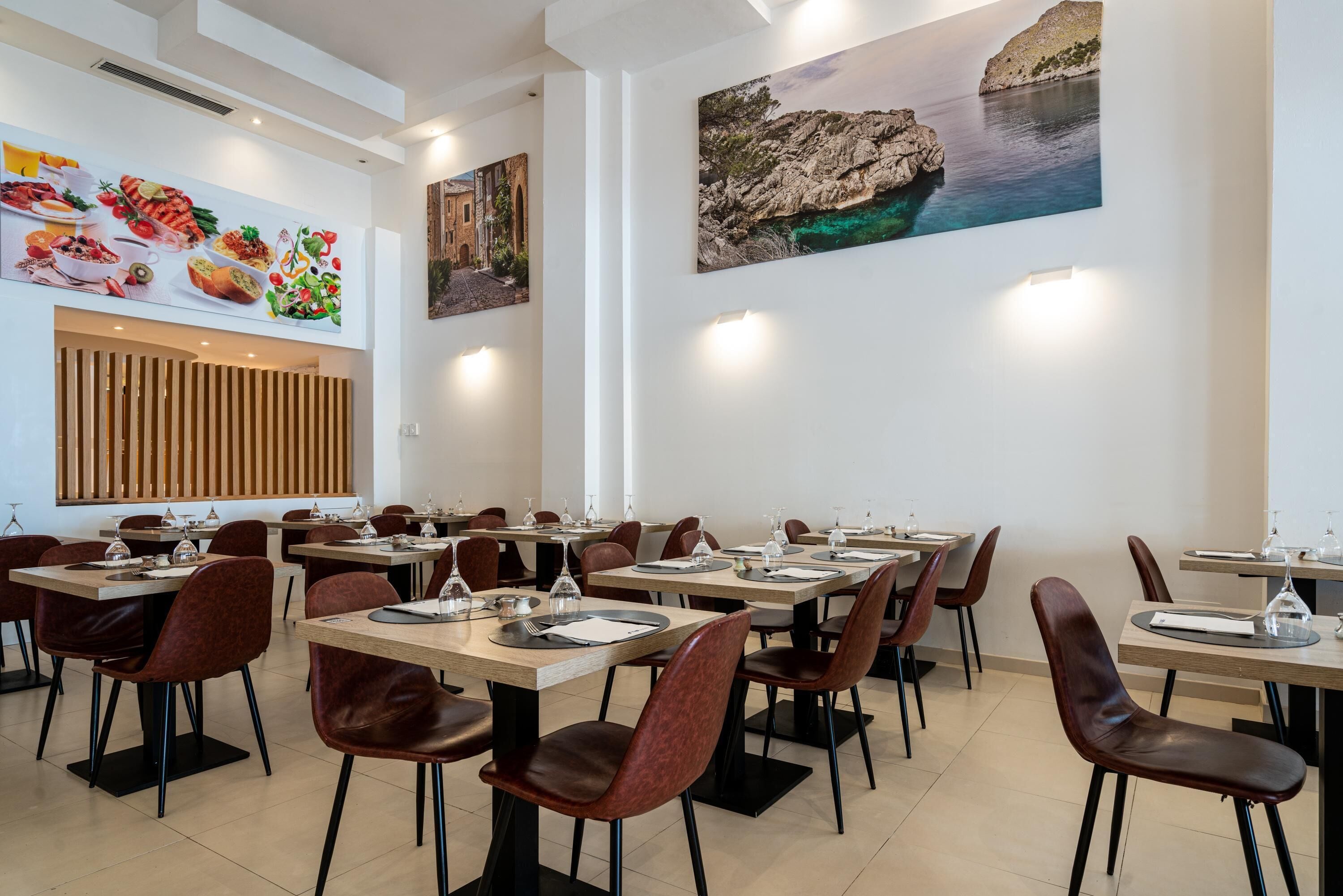 Un restaurant doté de nombreuses tables et chaises, d’une grande fresque murale représentant des aliments et d’un tableau représentant un paysage côtier.