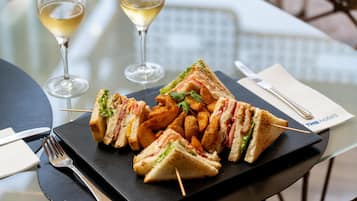 A table with a plate of sandwiches and fries, two wine glasses, cutlery, and a THB hotels napkin.