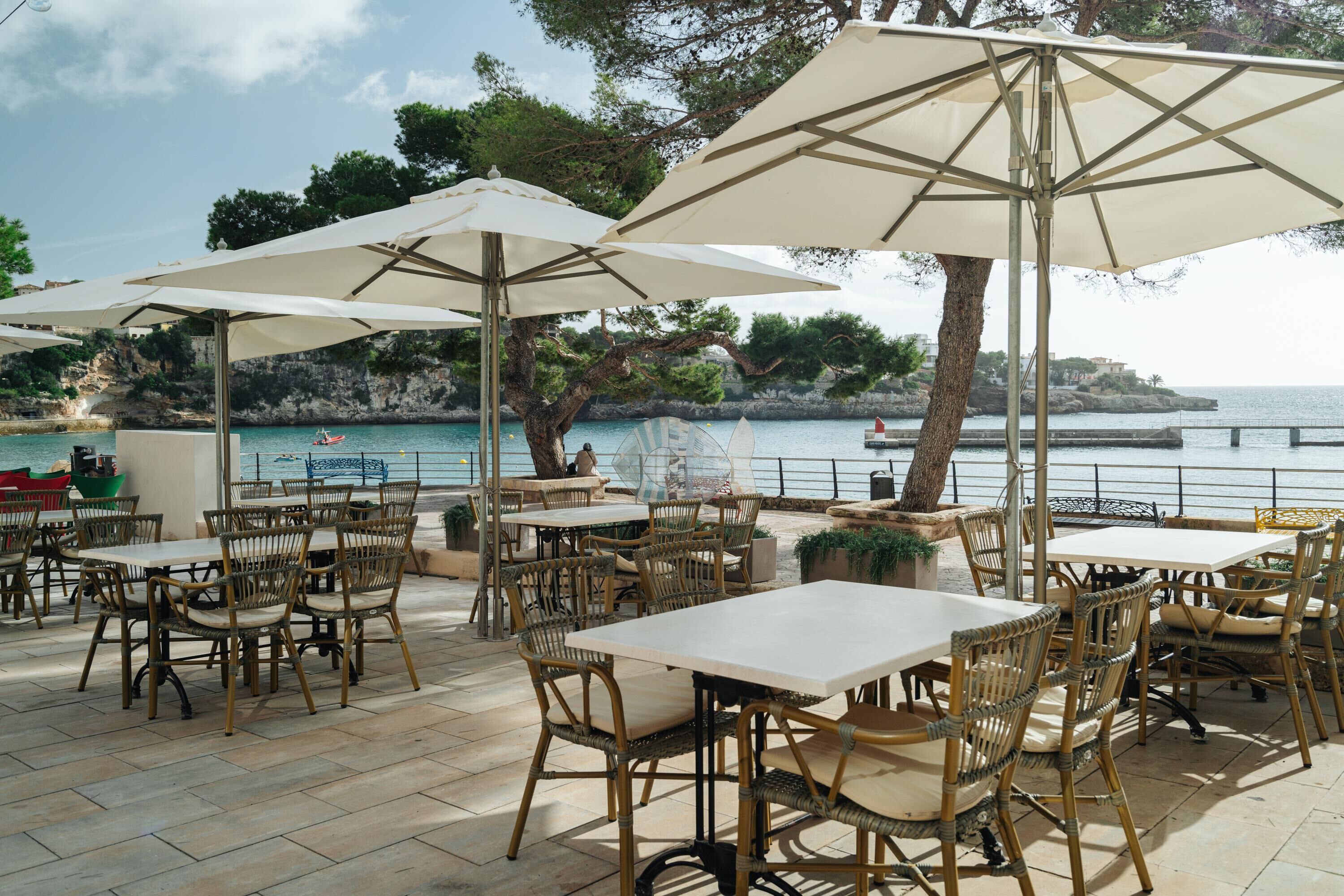 An outdoor seating area with tables and chairs, overlooking a body of water and rocky coastline.