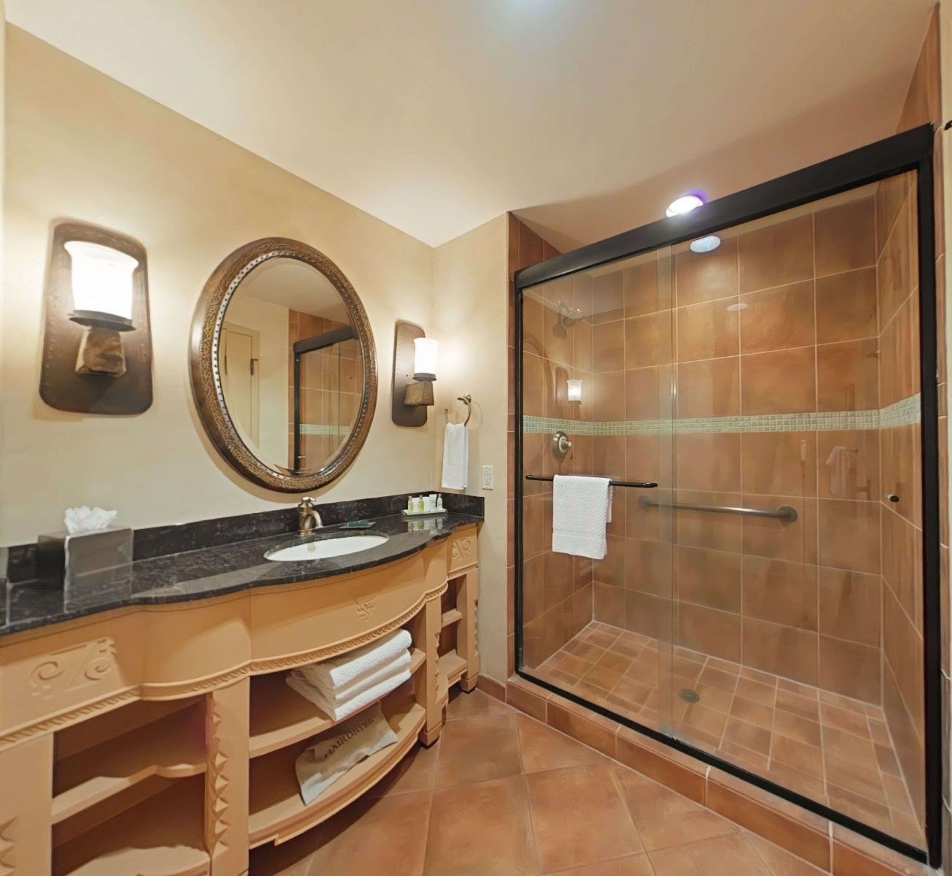 A bathroom with a large mirror, a sink, and a glass-enclosed shower.