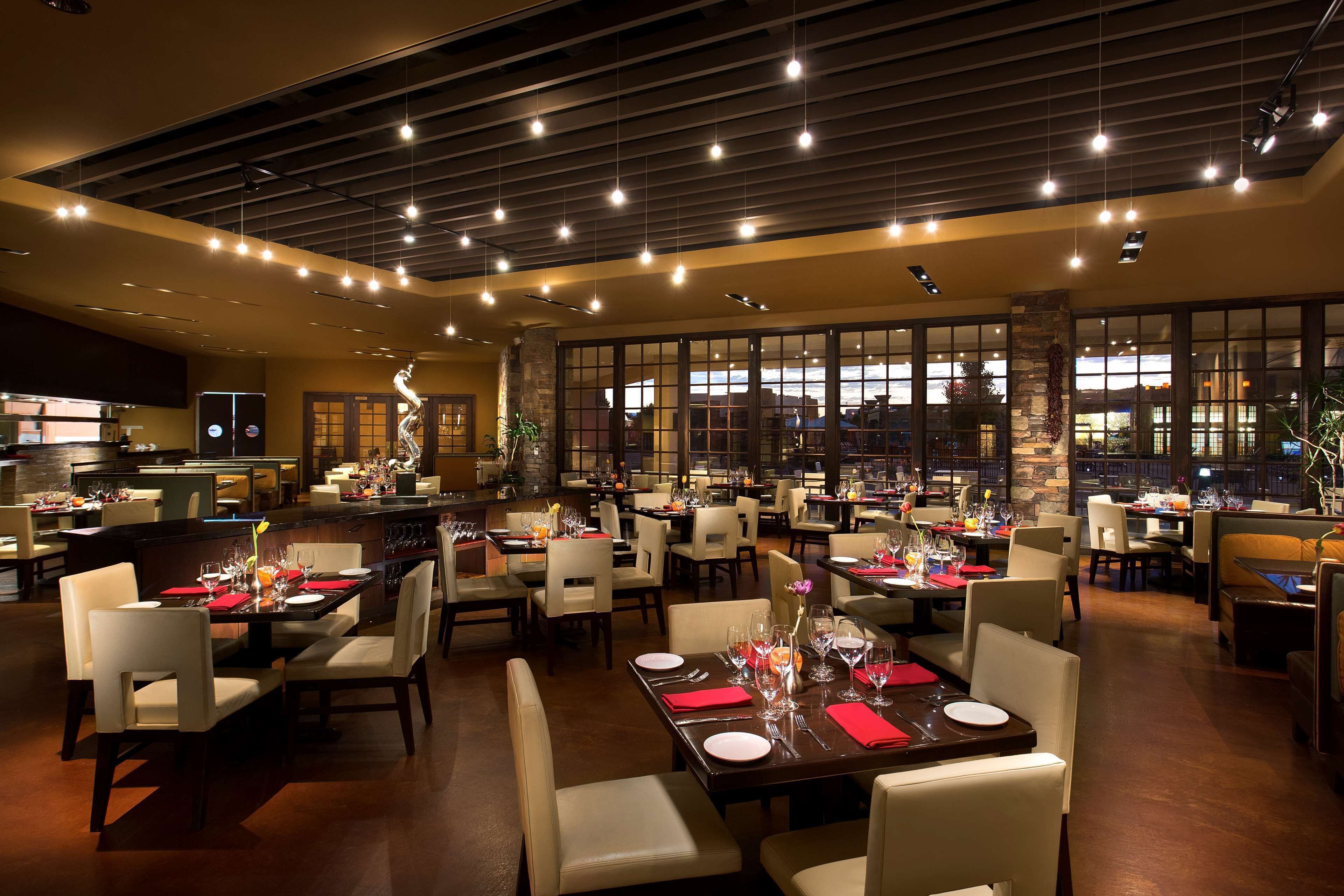 A spacious restaurant with multiple dining tables and chairs, large windows, and a modern ceiling design.