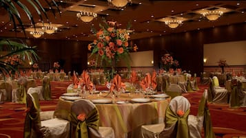 A banquet hall with round tables set for a formal event, featuring floral centerpieces and neatly arranged table settings.