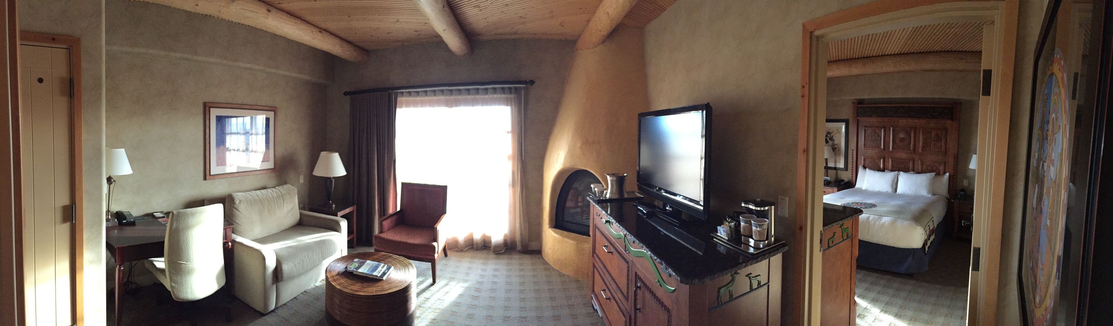 A hotel room with a bed, a desk, a chair, a TV, and a fireplace.