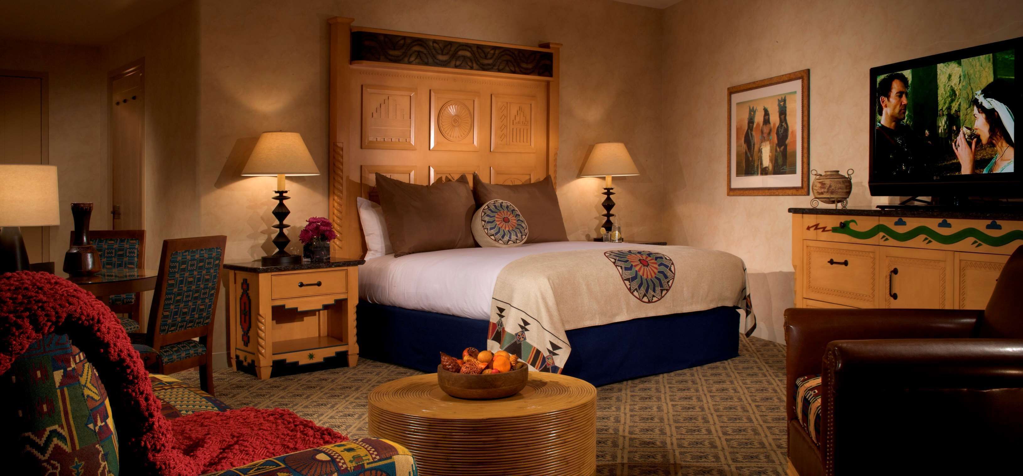 A hotel room with a large bed, two bedside tables with lamps, a television, a wooden cabinet, and a patterned rug.