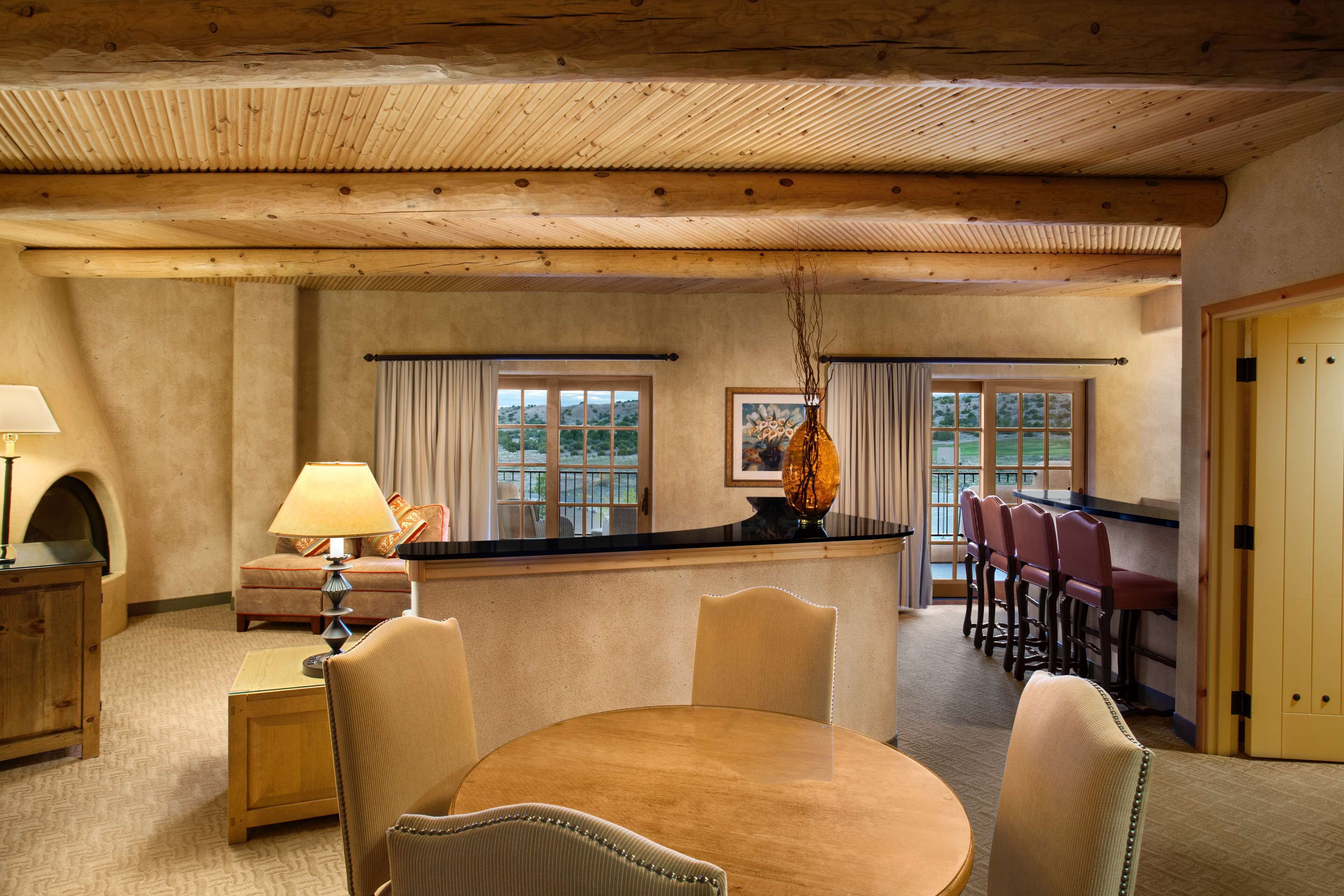 Un comedor acogedor con una mesa y sillas de madera, una barra con taburetes y vistas al exterior a través de grandes ventanales.