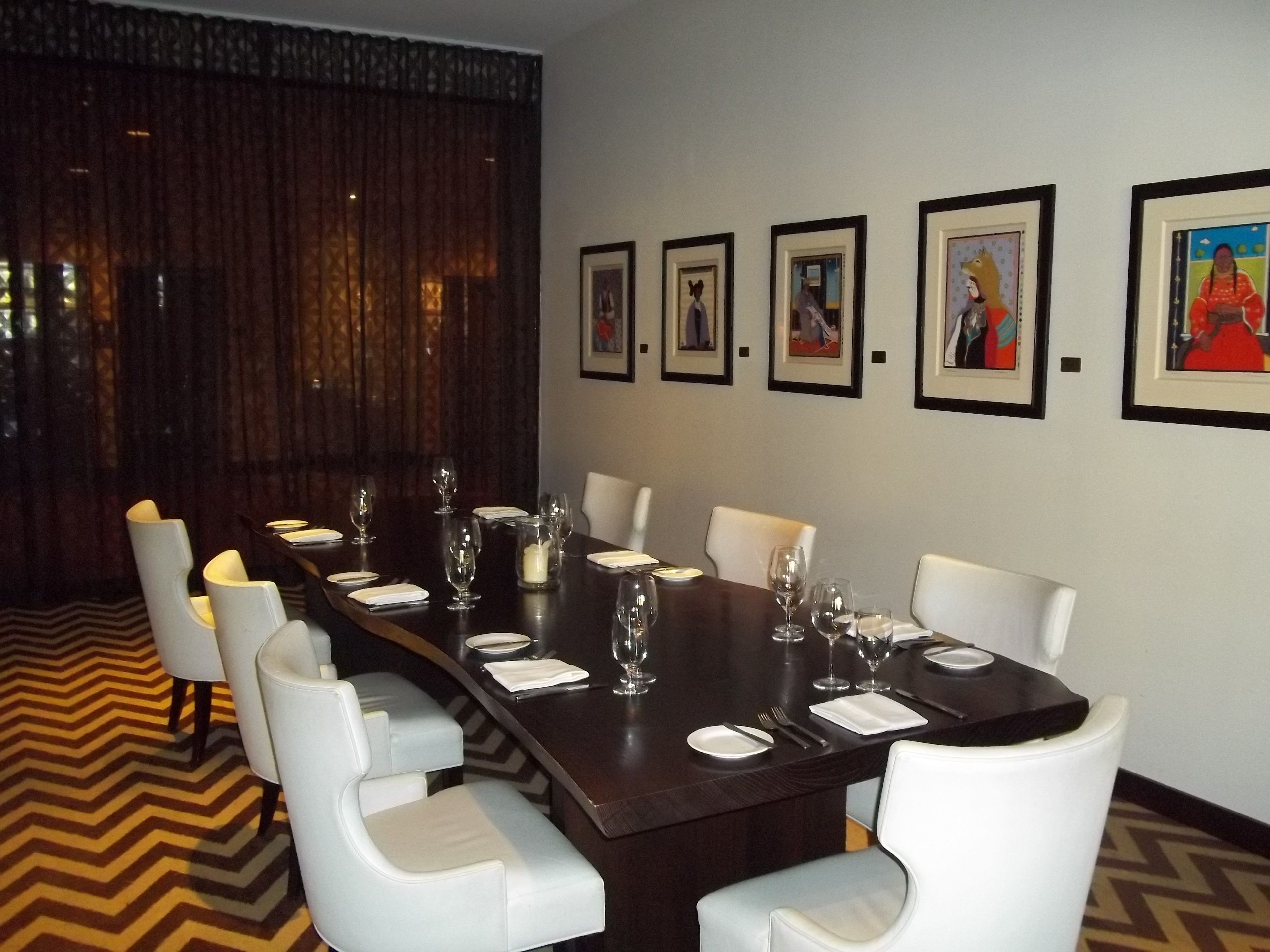A conference room with a long table, white chairs, and framed pictures on the wall.