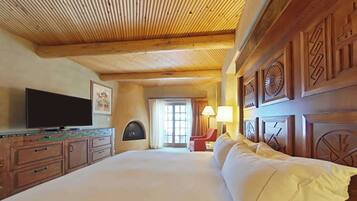 A large bed with white linens, a television on a wooden cabinet, a fireplace, and a window with curtains.