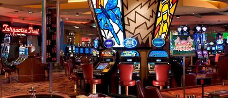 Une salle de casino avec des machines à sous, une table de roulette et un panneau au néon indiquant « Turquoise Trail ».
