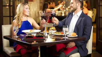 A couple dining at a restaurant with multiple dishes on the table, including wine glasses and a vase with red berries.