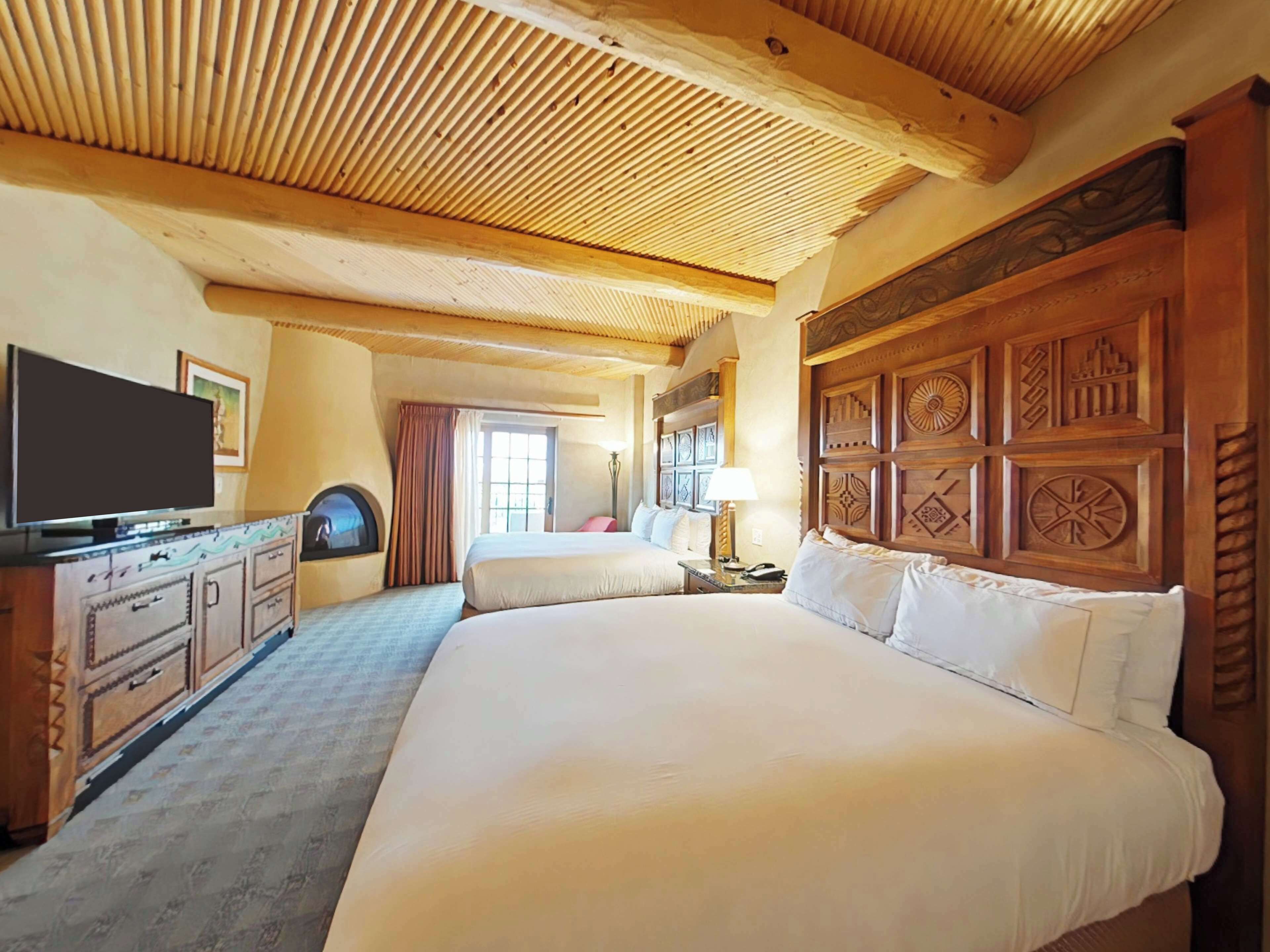 A hotel room with a large bed, a television, a dresser, and a window with curtains.