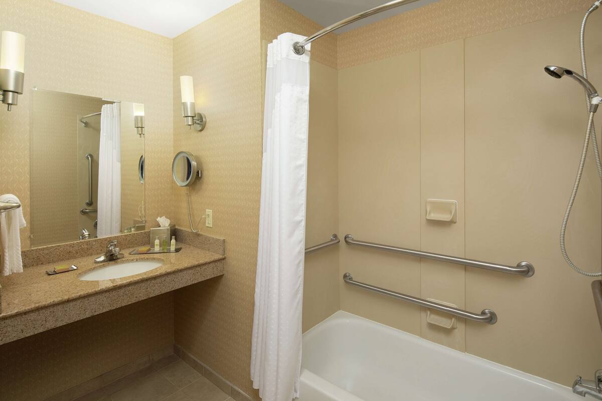 Un baño con dos lavamanos, ducha con barra de apoyo y bañera blanca.