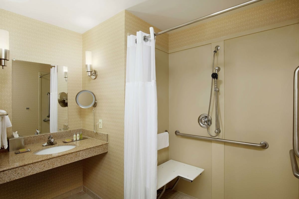 Baño con lavamanos, espejo, ducha y barras de apoyo.