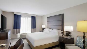A hotel room with a bed, bedside tables, a desk, a chair, a TV, and a window with curtains.
