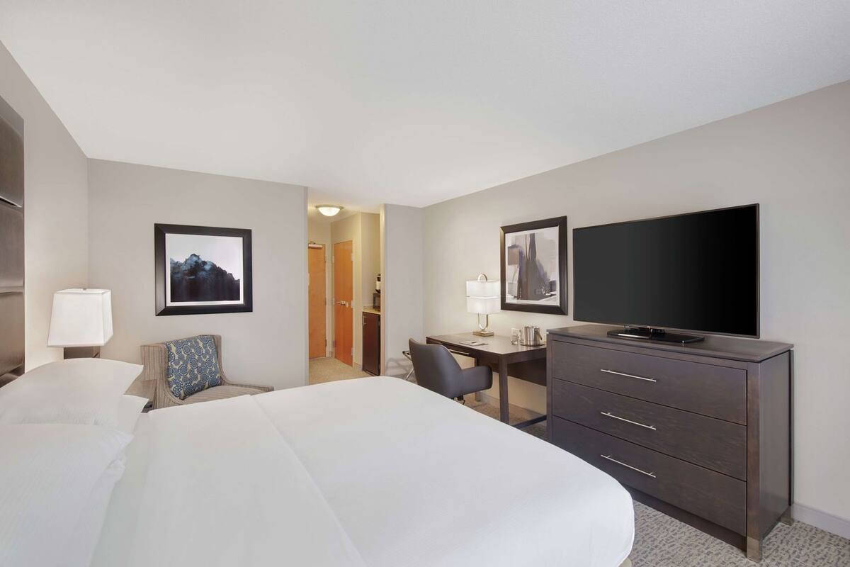 Habitación de hotel con dos camas, un escritorio, un televisor y cuadros en las paredes.