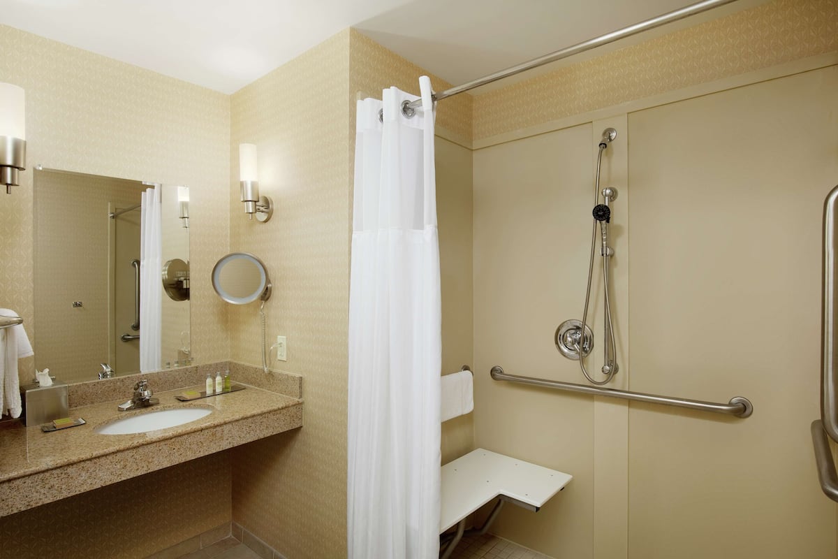 Un baño con lavabo, espejo, ducha y barras de apoyo.