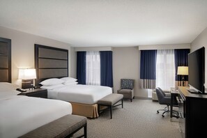 A hotel room with two beds, a desk, a chair, and a television.