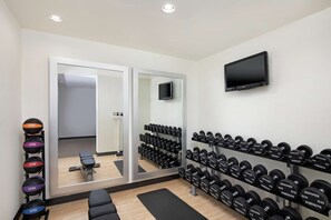 A gym with a mirrored wall, a TV, and neatly arranged dumbbells. - DoubleTree by Hilton Richmond Airport (Sandston)
