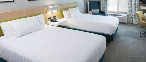 Habitación de hotel con dos camas, un escritorio, una silla y una ventana con cortinas.