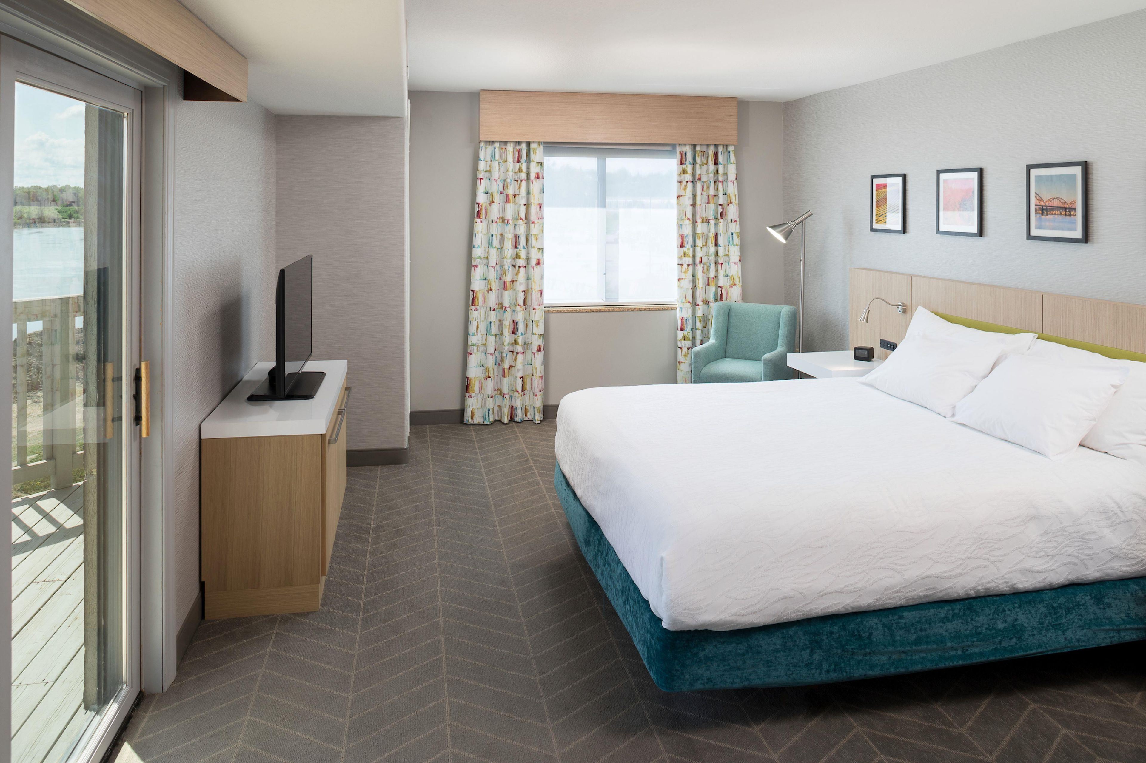A hotel room with a bed, a desk, a chair, a TV, and a window with curtains.