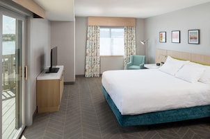 A hotel room with a bed, a desk, a chair, a TV, and a window with curtains.