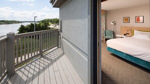 Habitación de hotel con balcón y vista a un cuerpo de agua, cama, escritorio y una silla.