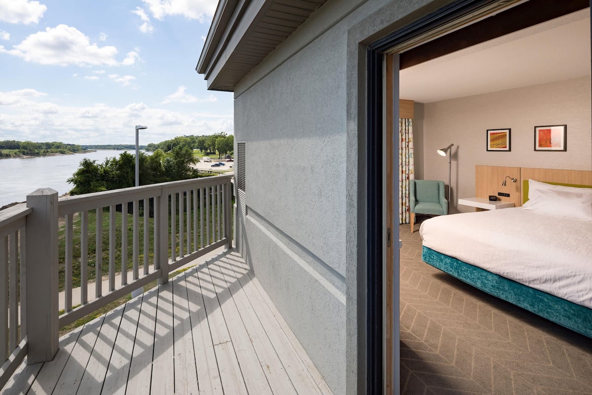 Ein Hotelzimmer mit Balkon und Blick auf ein Gewässer, inklusive Bett, Schreibtisch und Sessel.