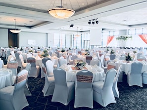 Une salle de banquet avec des tables rondes, des chaises blanches et une scène.