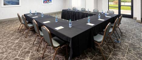 Un salón de conferencias con una mesa larga, sillas, botellas de agua y vistas al exterior a través de una puerta.