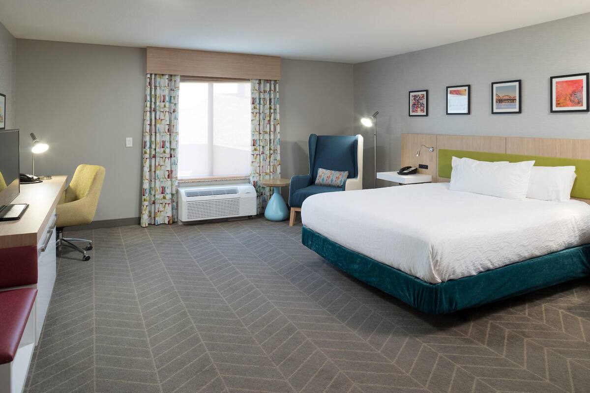 Ein Hotelzimmer mit Bett, Schreibtisch, Stuhl und einem kleinen Tisch mit Lampe.