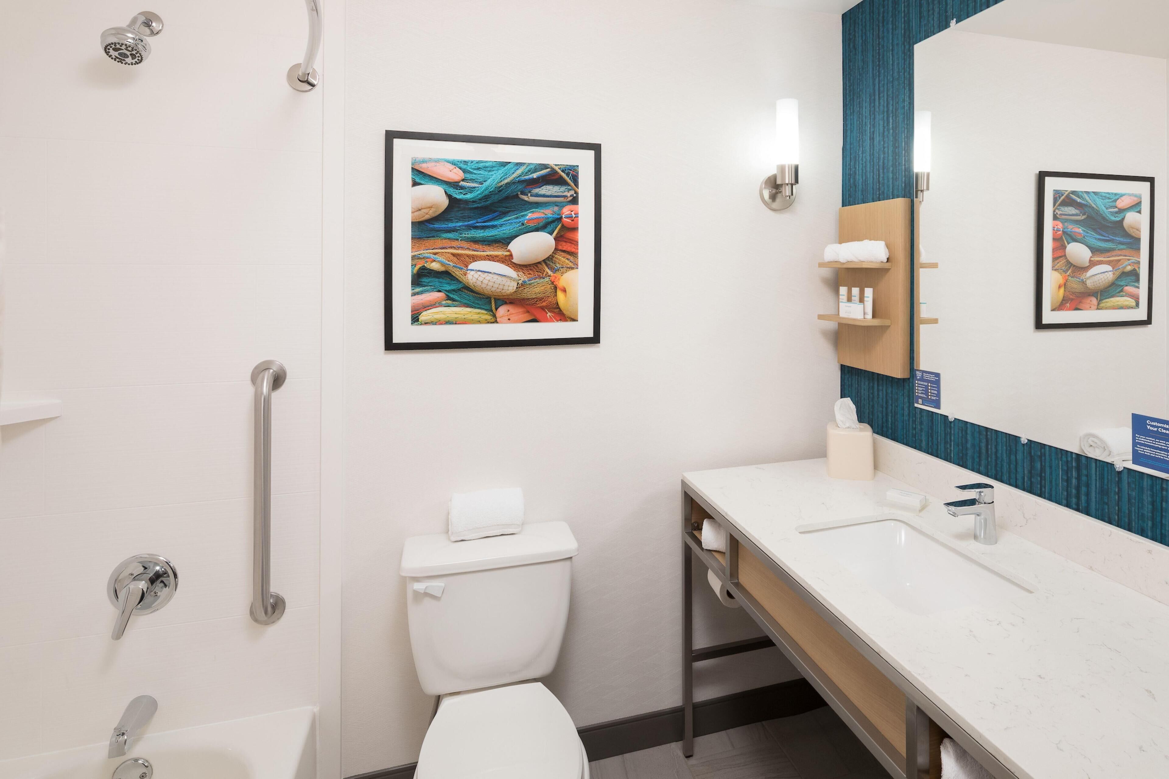 Une salle de bain moderne équipée de toilettes, d’un bidet et d’un lavabo. Les murs sont ornés d’œuvres d’art encadrées et un miroir est placé au-dessus du lavabo.