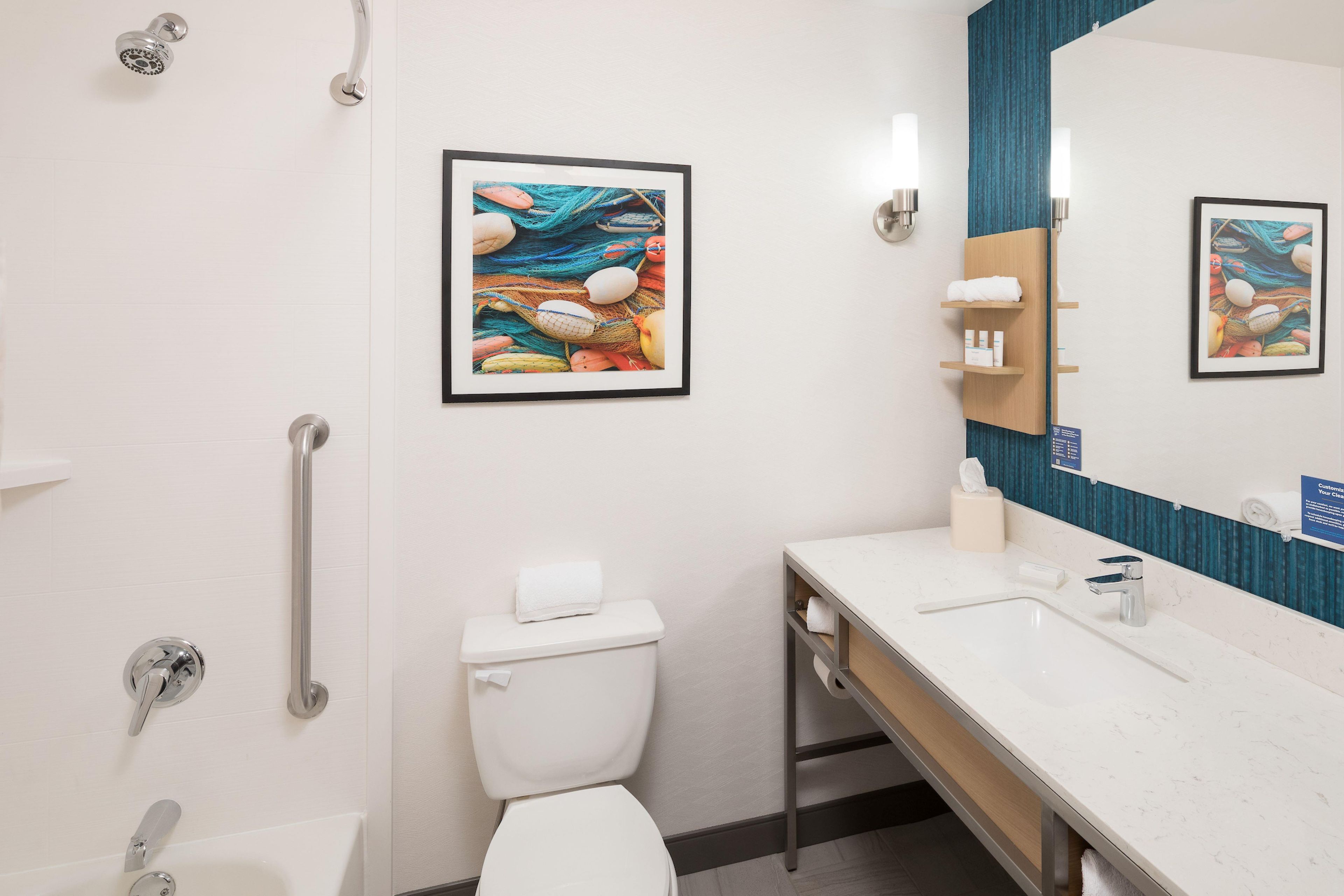 Un baño moderno con inodoro, bidé y lavamanos con espejo. Hay cuadros enmarcados en la pared y un perchero para toallas.