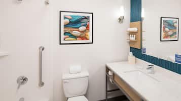 Un baño moderno con inodoro, bidé y lavamanos con espejo. Hay cuadros enmarcados en la pared y un perchero para toallas.