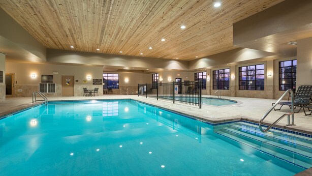 Una piscina interior con techo de madera, ventanas de vidrio transparente y suelo de baldosas.