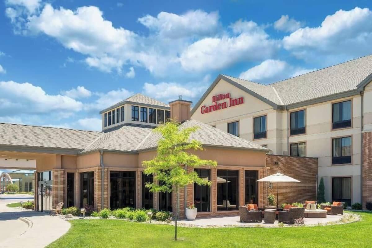 Ein Hotel mit Garten-Terrasse, einem Schild mit der Aufschrift 'Hilton Garden Inn' und blauem Himmel.